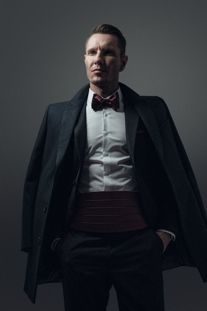 Stylish portrait of a man in formal wear with an overcoat and bow tie in a studio setting.