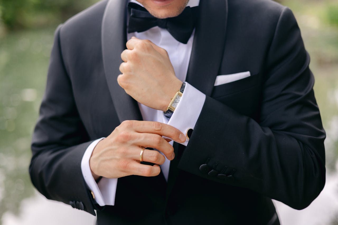 Close-up of a well-dressed man adjusting his cufflinks, showing a gold wristwatch and wedding ring.