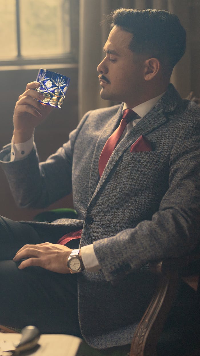 A sophisticated man enjoying a glass of whiskey indoors, showcasing modern style and luxury.