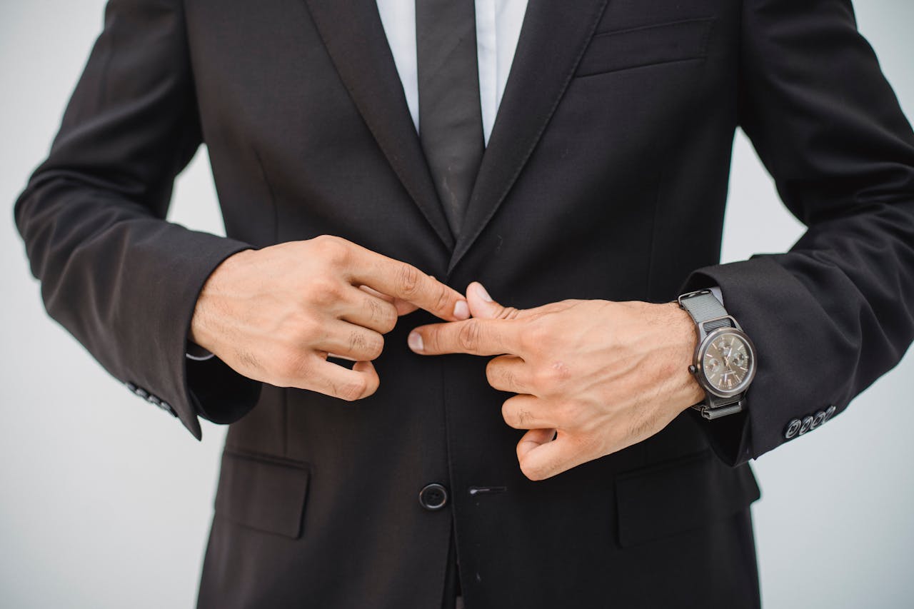 services-03 Close-up of a man's hands adjusting a black suit jacket, showcasing confidence and style.
