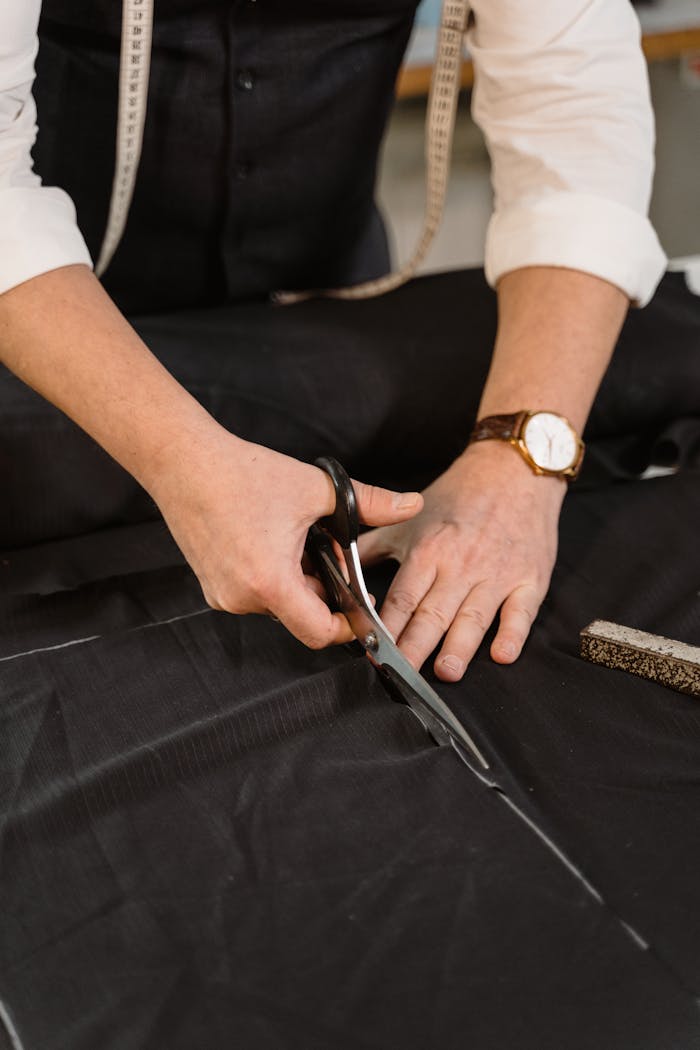 about-01 Close-up of a professional tailor carefully cutting black fabric in a workshop.