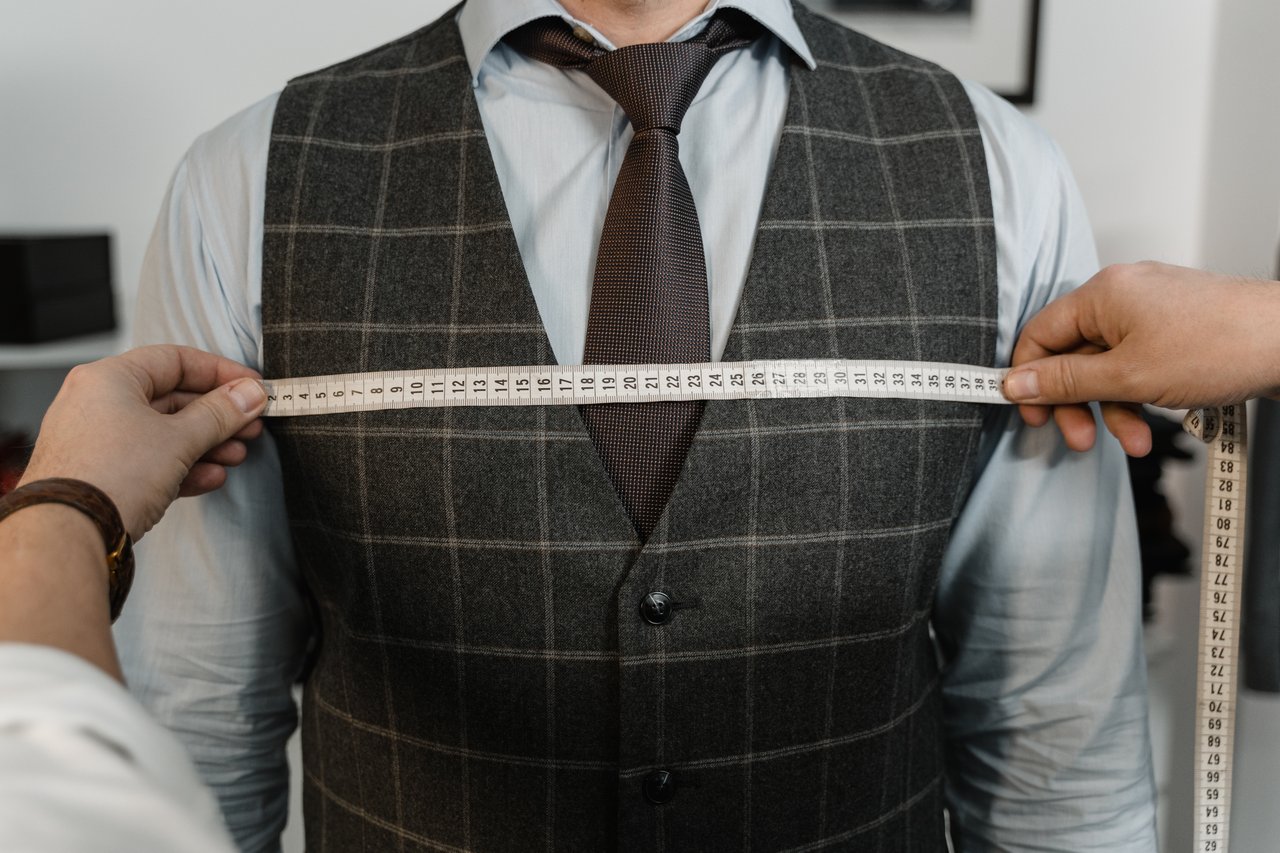 services-img A tailor measuring a client's chest for a bespoke suit in a professional setting.